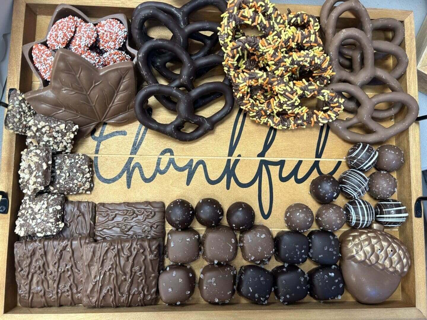 A tray of assorted chocolates and pretzels with the word " thankful ".