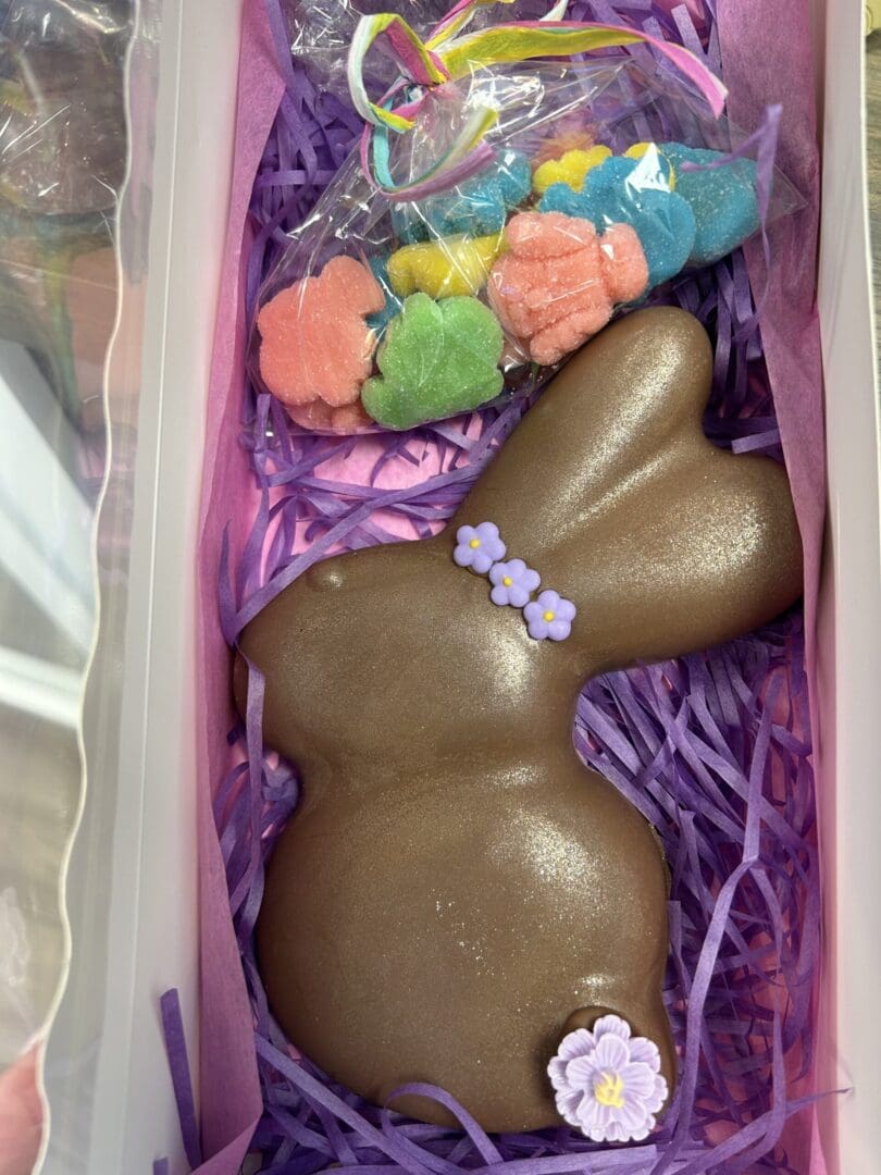 Chocolate bunny with colorful flower candies in a gift box.