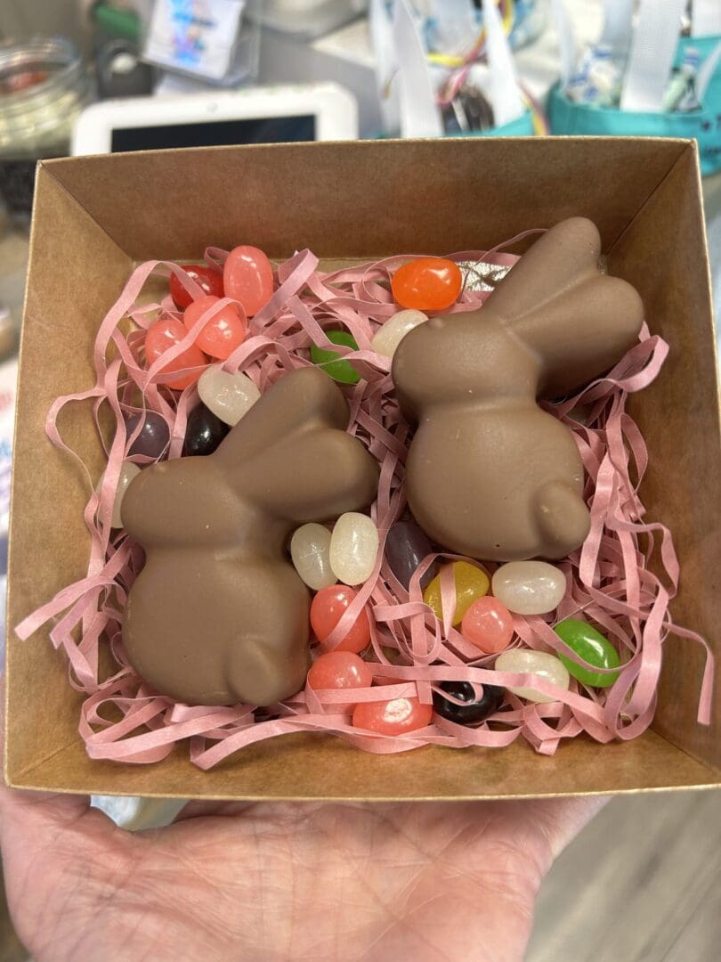 Three chocolate bunnies surrounded by colorful candy in a box.