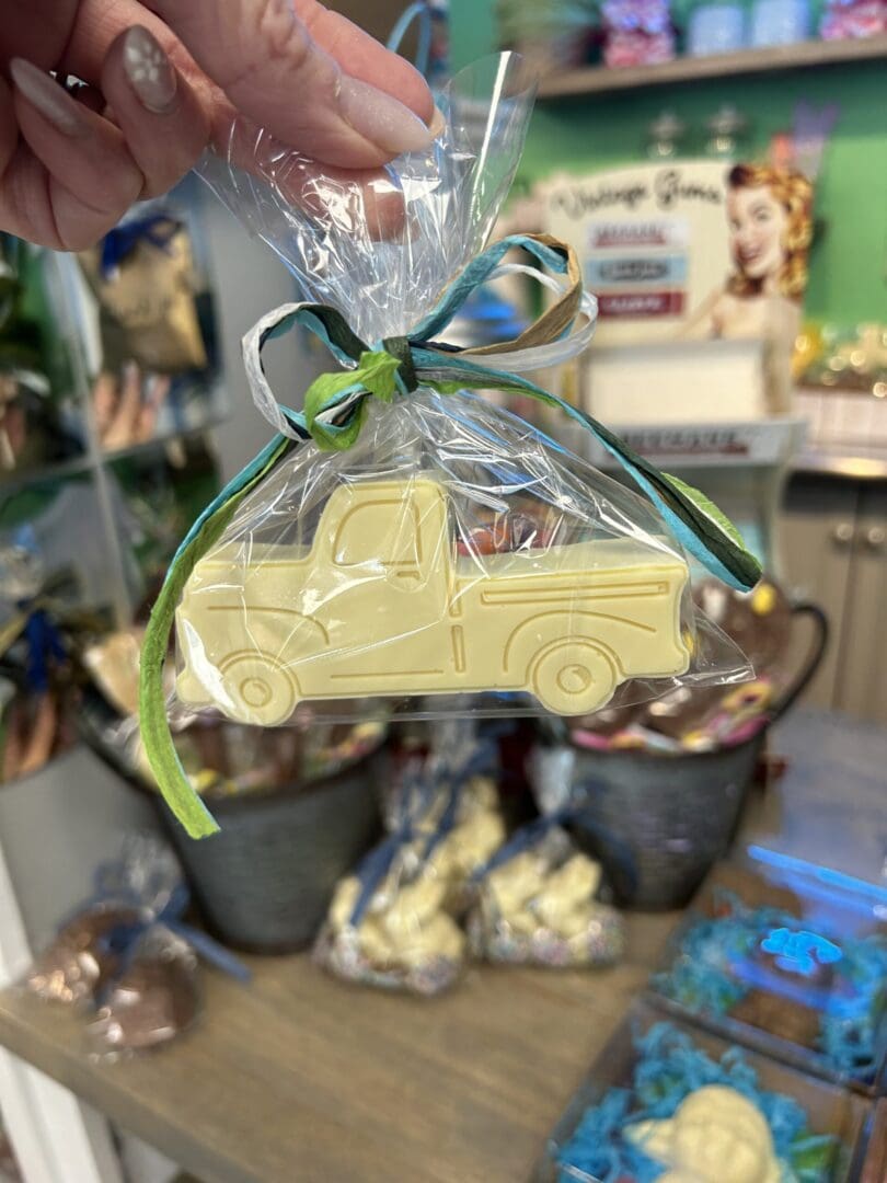 A yellow car-shaped cookie wrapped in clear plastic with a blue and green ribbon.