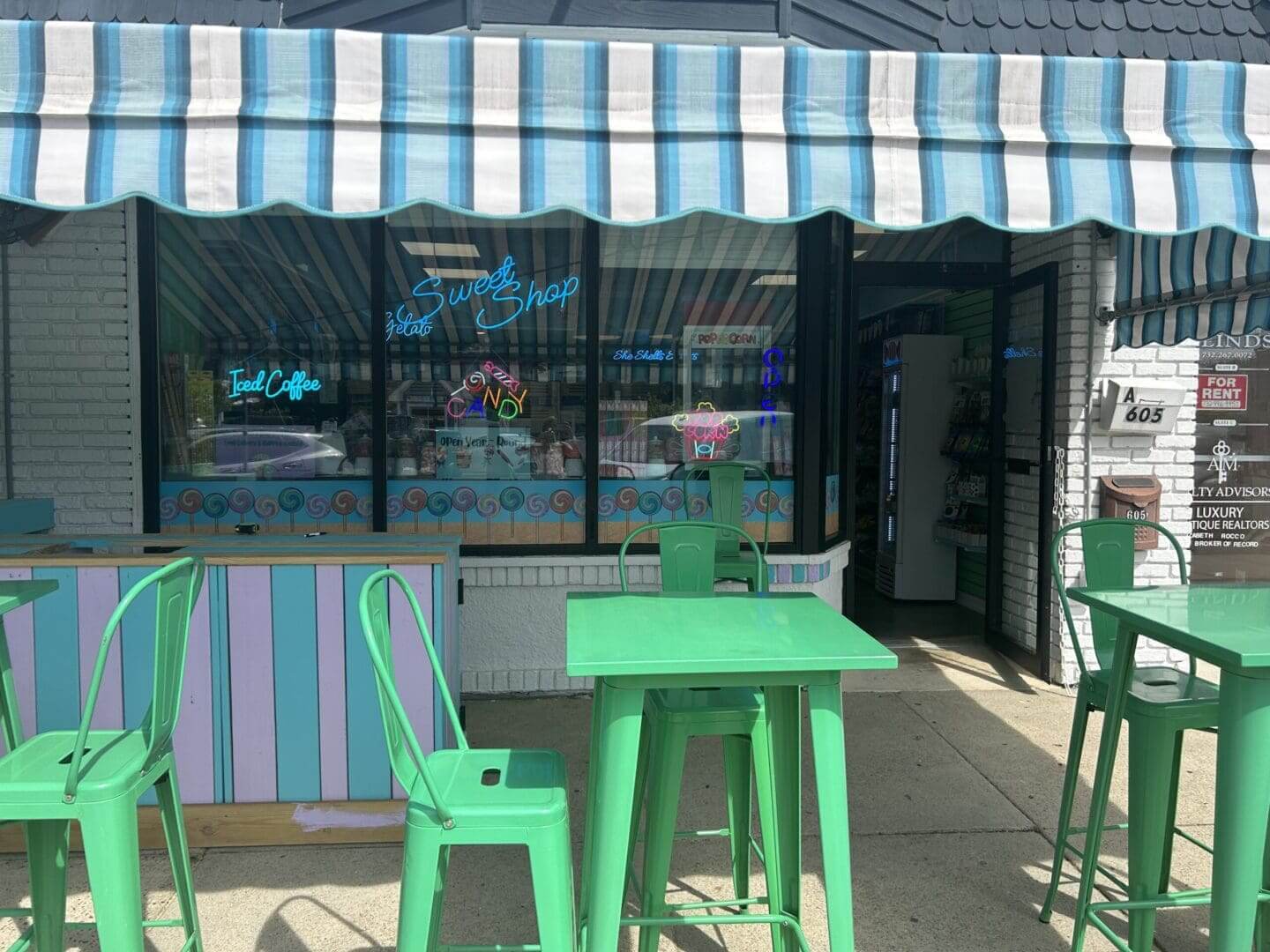 Outdoor green table and stools under a blue-striped awning.