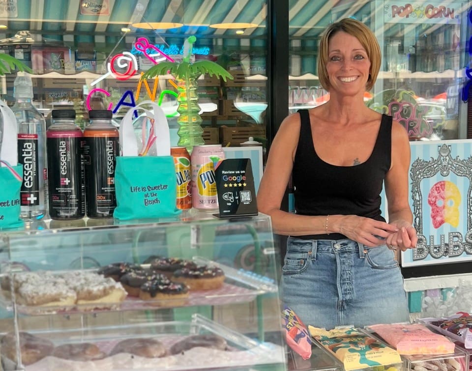 Smiling woman behind a glass display case of desserts in a bakery.